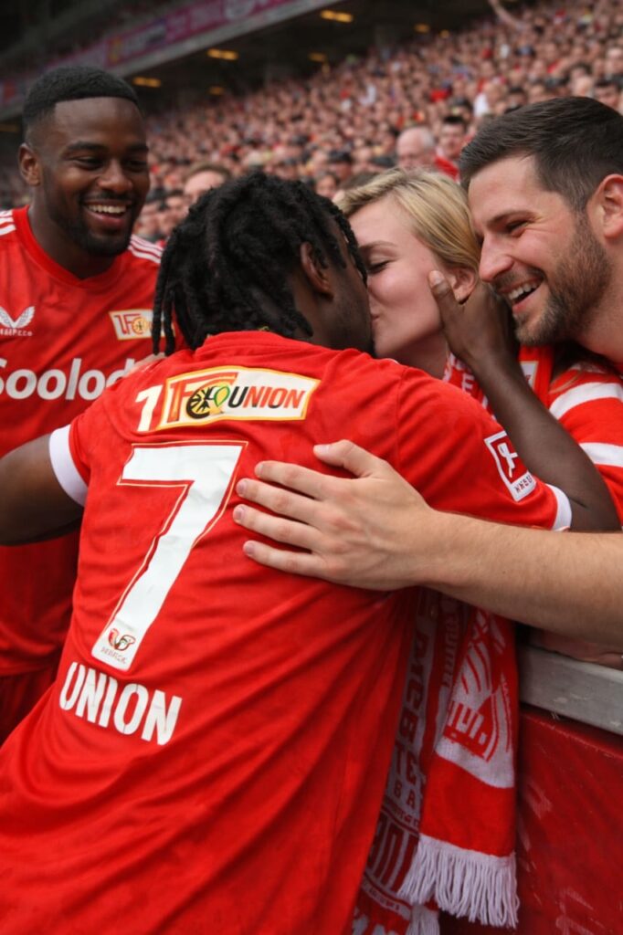 Was für ein Wahnsinn im Stadion: Ein Star von FC Union Berlin sorgt nach einem traumhaften Treffer für eine Szene, die niemand so schnell vergisst. Direkt nach seinem spektakulären Tor sprintet der Publikumsliebling an den Spielfeldrand, springt auf die Bande und drückt einem völlig überraschten Fan einen spontanen Kuss auf. Ekstase, Emotionen und pure Leidenschaft – dieser Moment zeigt, wie Fußball Herzen verbindet und eine ganze Arena in Ausnahmezustand versetzt. Ein Bild, das Fans weltweit begeistert und für Gänsehaut sorgt.